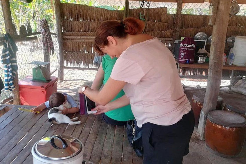 A woman and a child interacting with a tablet on a wooden table in a rustic outdoor setting. 4