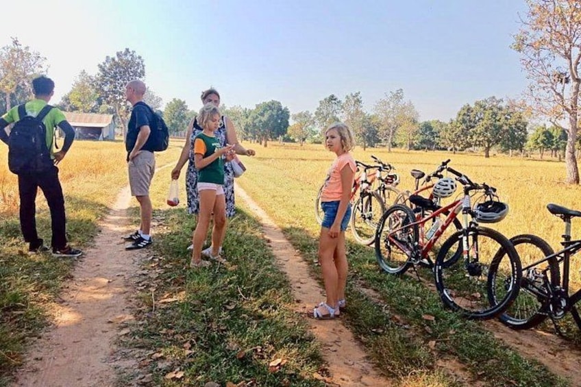 A group of people standing on a dirt path in a grassy field with bicycles parked nearby. 2