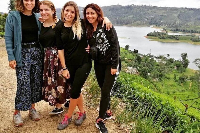 Four people standing on a dirt path with a lake and greenery in the background. 3
