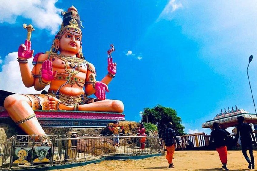 A large statue of a deity with multiple arms, a pedestal, and a fence in the foreground. 5