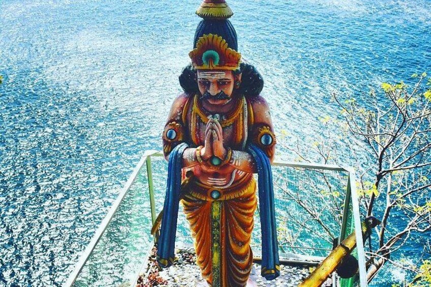 A statue of a deity with a blue and orange robe, standing on a platform with a railing, overlooking a body of water. 2