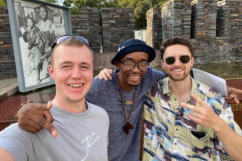 Three people posing in front of a stone wall and a framed picture. 1