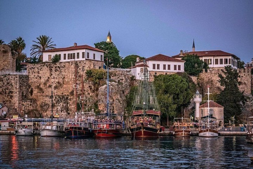 A harbor with boats, a stone wall, and buildings on a cliff. 1