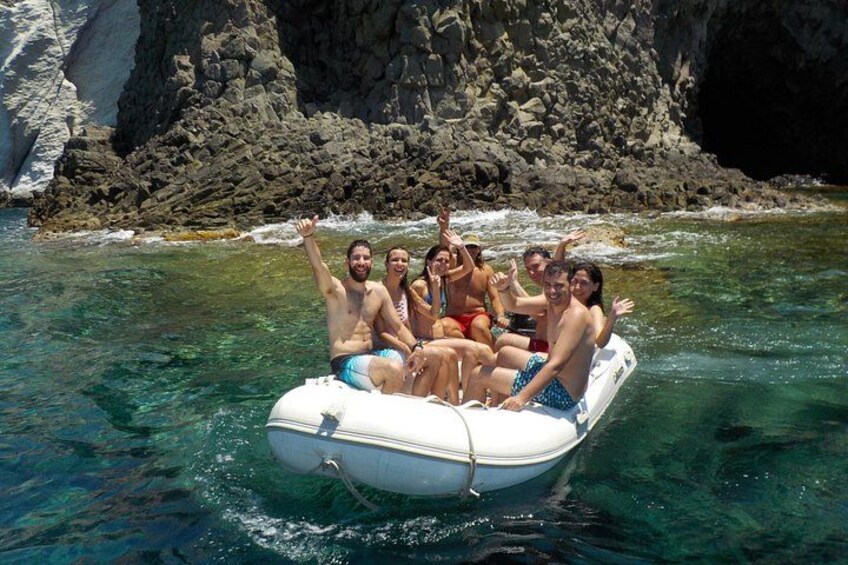 Eine Gruppe von Menschen in einem weißen Schlauchboot auf klarem Wasser, im Hintergrund steilen Felsen. 5