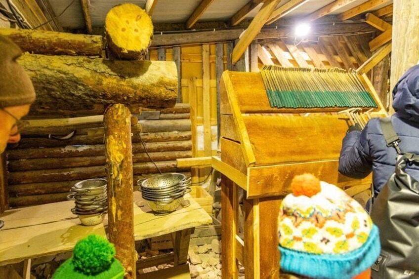 A wooden structure with a log press, metal bowls, and a person operating machinery. 2
