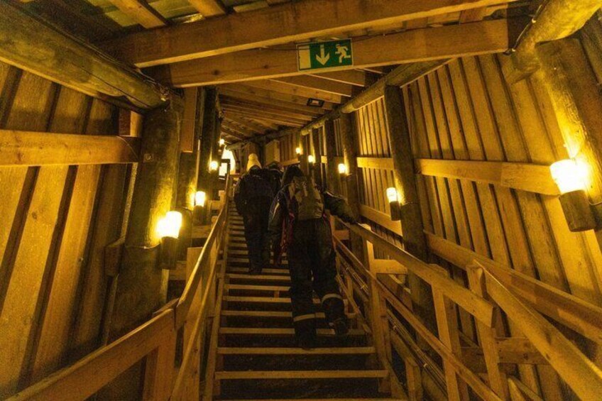 A wooden staircase with railings and overhead lighting, leading to an exit sign. 5