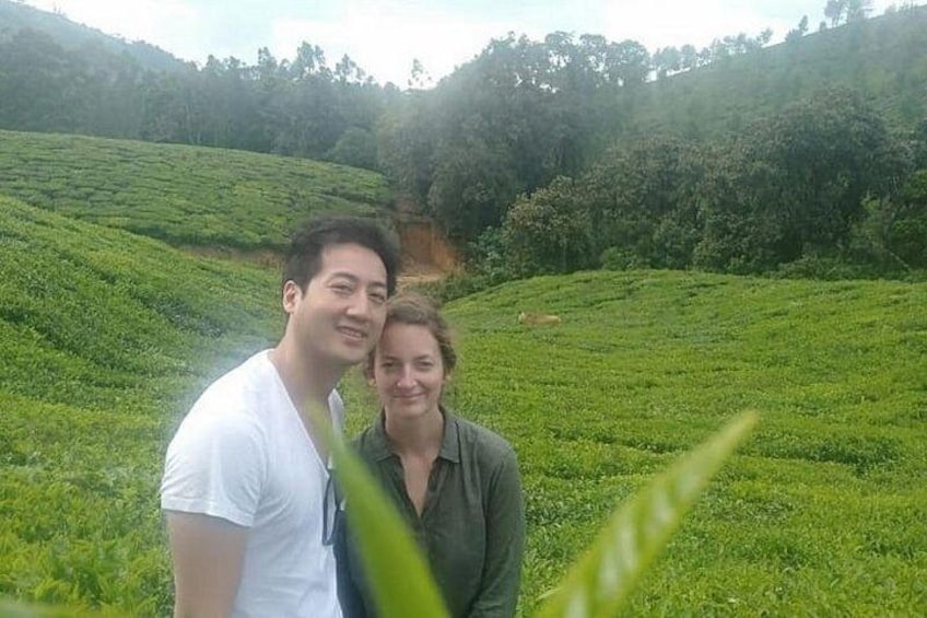 Two people standing in a lush green tea plantation with rolling hills in the background. 1