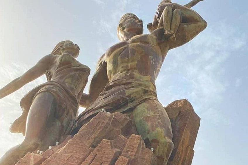 Een standbeeld van twee figuren, één zittend en één staand, op een rotsachtige richel met een heldere lucht op de achtergrond. 1