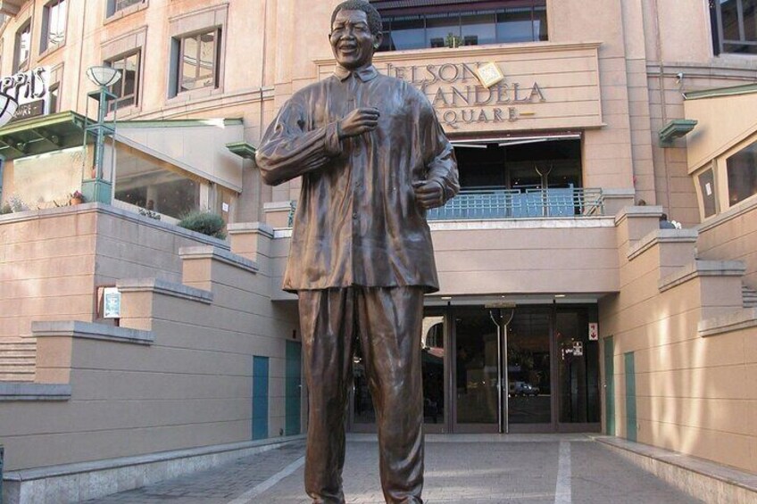 A statue of Nelson Mandela in front of a building with a sign that reads "Nelson Mandela Square". 1