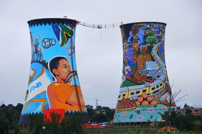 Two large cooling towers with colorful murals, one depicting a man with a microphone and the other showing a family with a car. 4