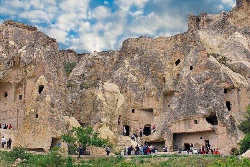 Paesaggio roccioso con abitazioni rupestri scolpite e un gruppo di persone. 5