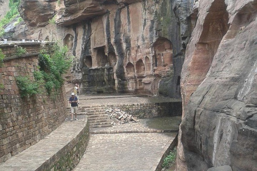 A rock formation with carved niches and a paved walkway. 2