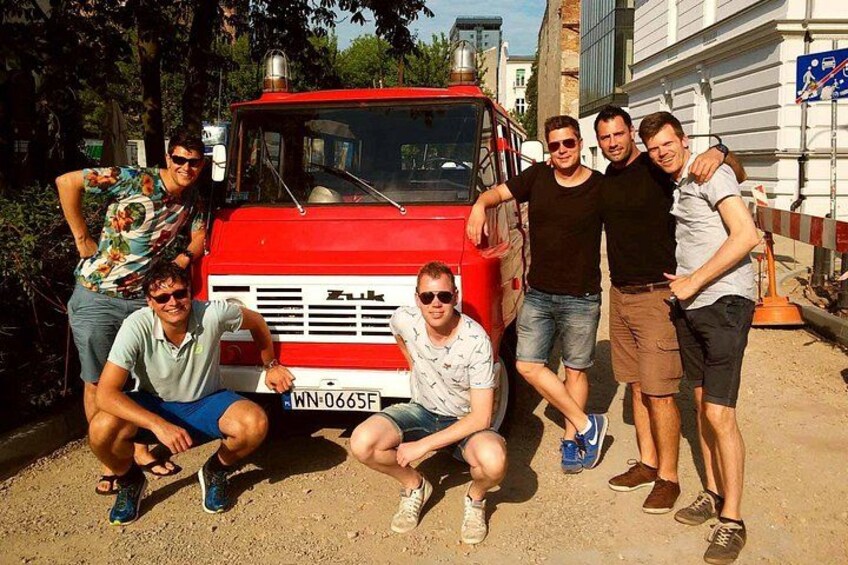 A group of people posing in front of a red truck with a license plate. 5