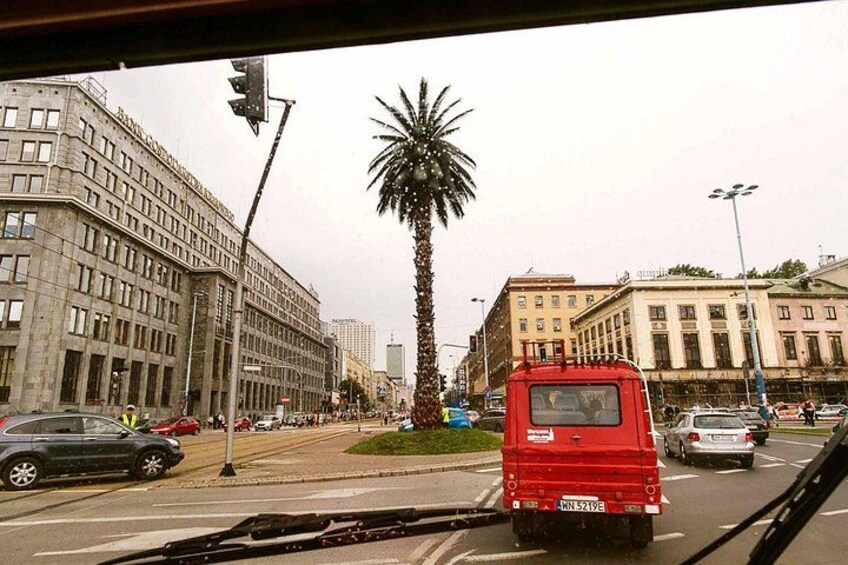 A busy urban street with a red bus, palm trees, and historic buildings. 2