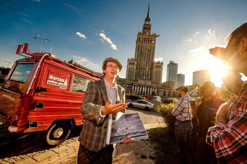 A red van with 'Warsaw' written on it, a person gesturing, and a tall building in the background. 3