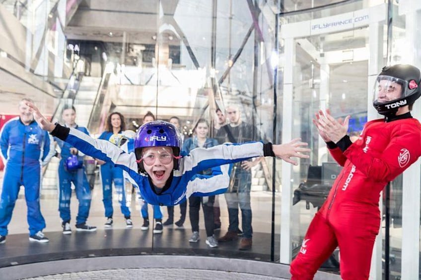 Une personne vêtue d’un costume bleu et blanc, portant un casque, se tient sur une plateforme circulaire, les bras tendus. 5