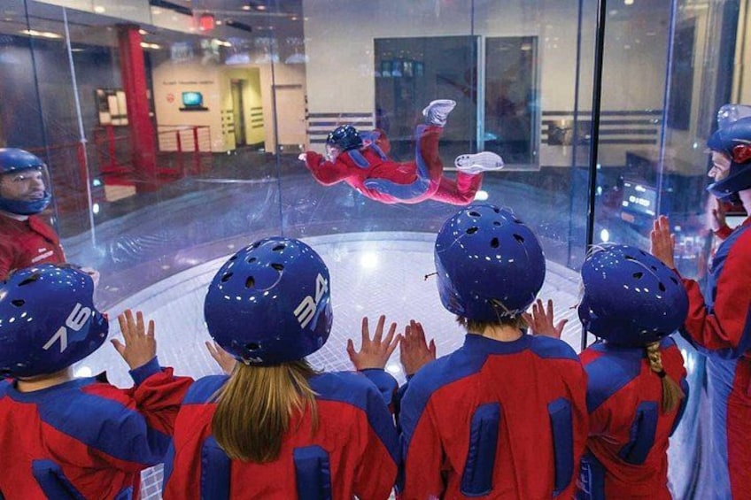 Des enfants, portant des casques rouges et bleus, regardent une patineuse artistique exécuter sa routine à l’intérieur d’une structureClose en verre. 2