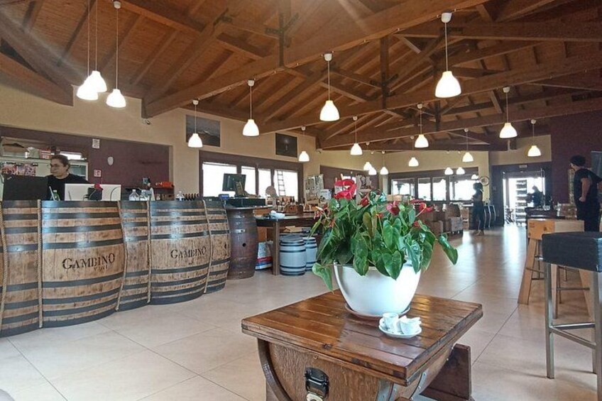 Un bar con barriles de madera etiquetados 'Gambino', un recipiente blanco grande con flores y lámparas colgantes. 2