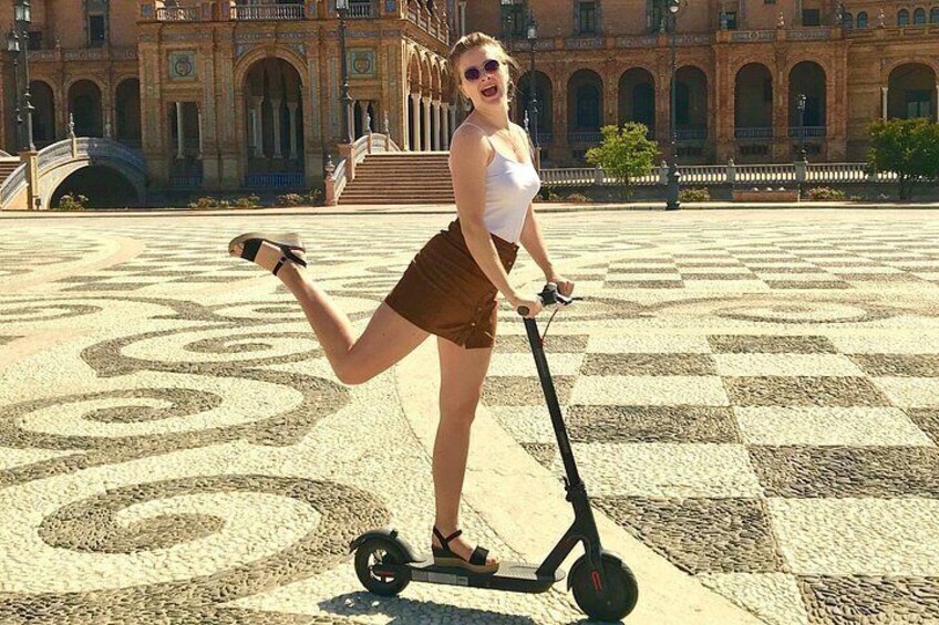 A person on a scooter in a plaza with patterned ground and a large building in the background. 3