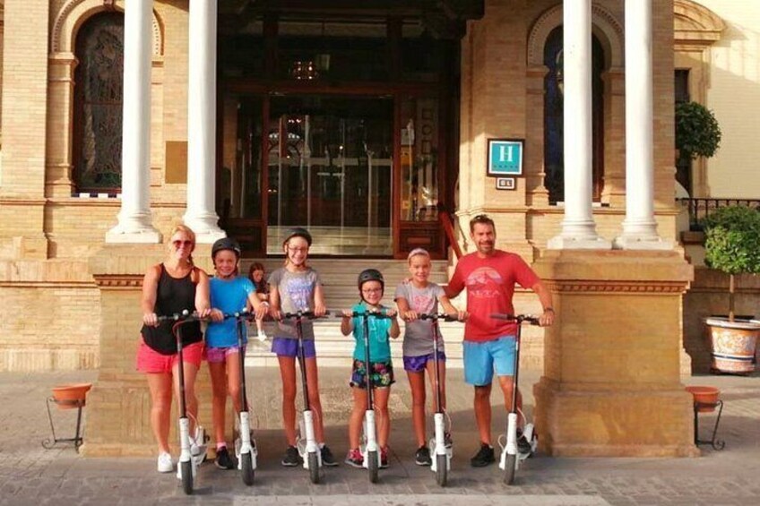 A group of people on scooters in front of a building with columns and a sign. 5