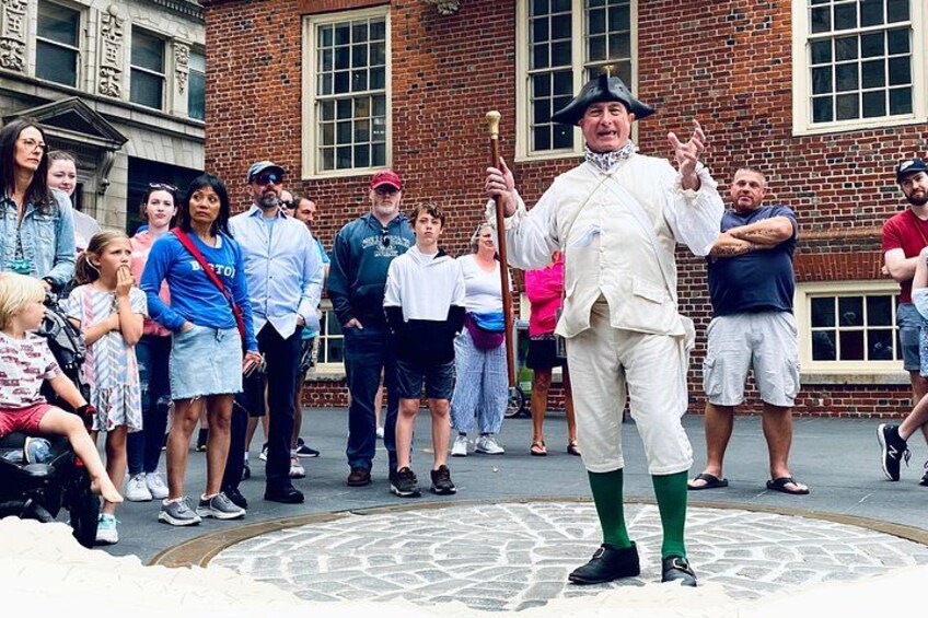 A person in historical costume standing on a cobblestone street with a crowd watching. 3