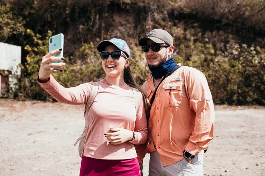 Deux personnes prennent un selfie à l’extérieur, avec un sol en terre et de la verdure en arrière-plan. 4