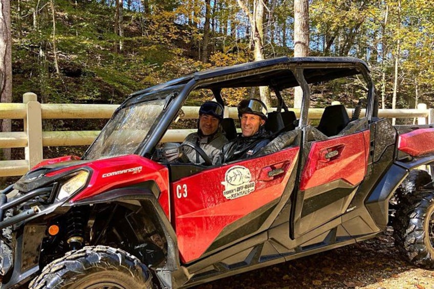 A red and black off-road vehicle with a logo on the side, parked in a wooded area. 1