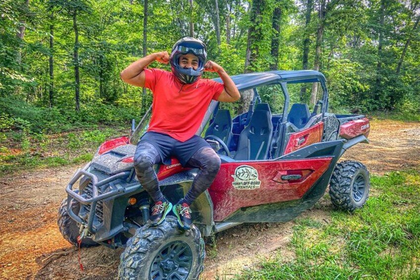 A person sitting on a red and black off-road vehicle in a forested area. 2
