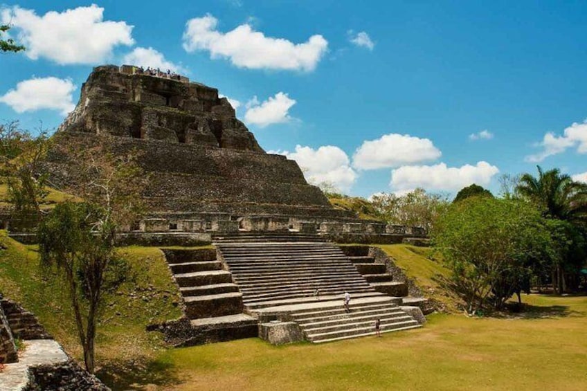 A large pyramid structure with a staircase leading up to it, surrounded by greenery and a clear sky. 1