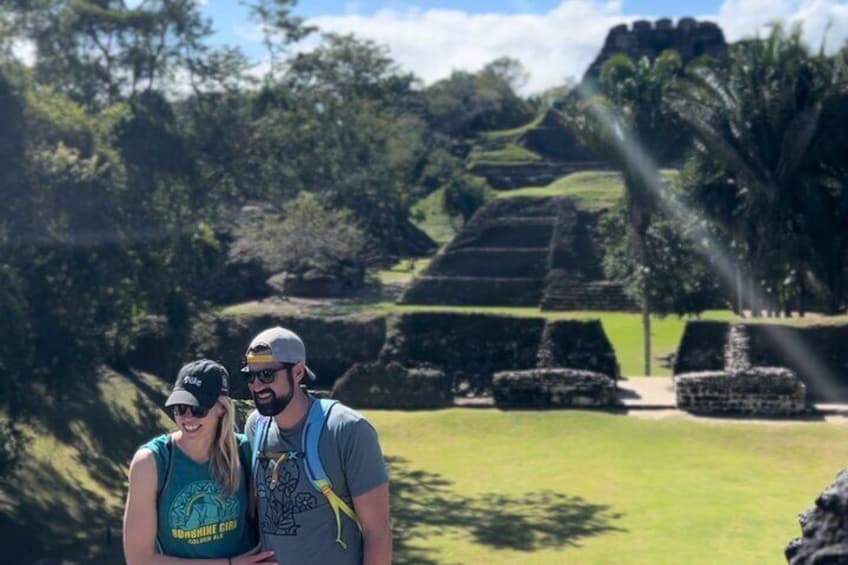 Two people standing in front of ancient ruins with stepped pyramids and lush greenery. 2