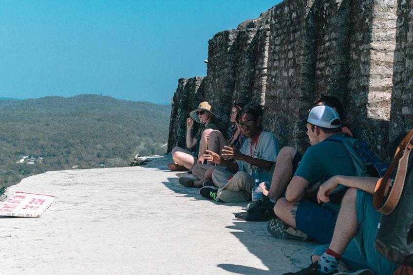 A group of people sitting on a stone ledge with a view of a mountainous landscape. 5