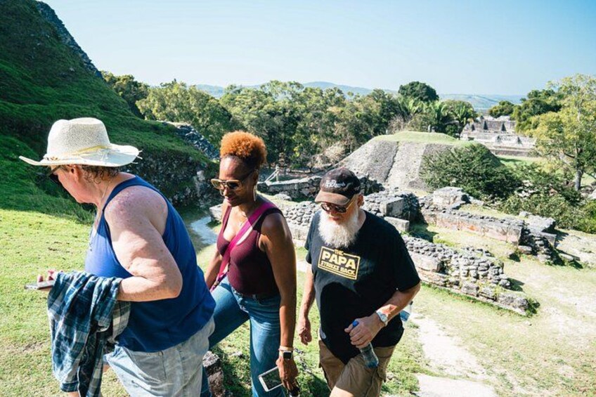 Three people standing near ancient ruins with a river and greenery in the background. 2