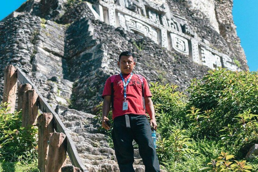 A person standing in front of a large rock with ancient carvings, surrounded by greenery. 4