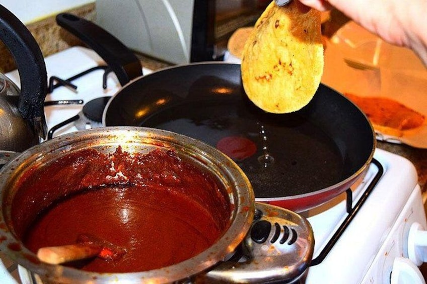 Une casserole de sauce rouge sur une cuisinière, une poêle et une main tenant une tortilla. 1