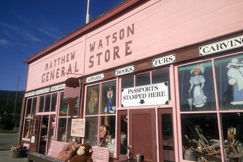 A pink building with signs for 'MATTHEW GENERAL STORE' and 'WATSON STORE' with various items like books, furs, and passports. 2
