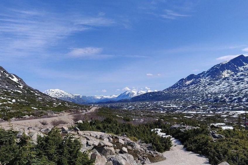 A mountainous landscape with a clear sky, a dirt path, and snow-capped peaks. 3