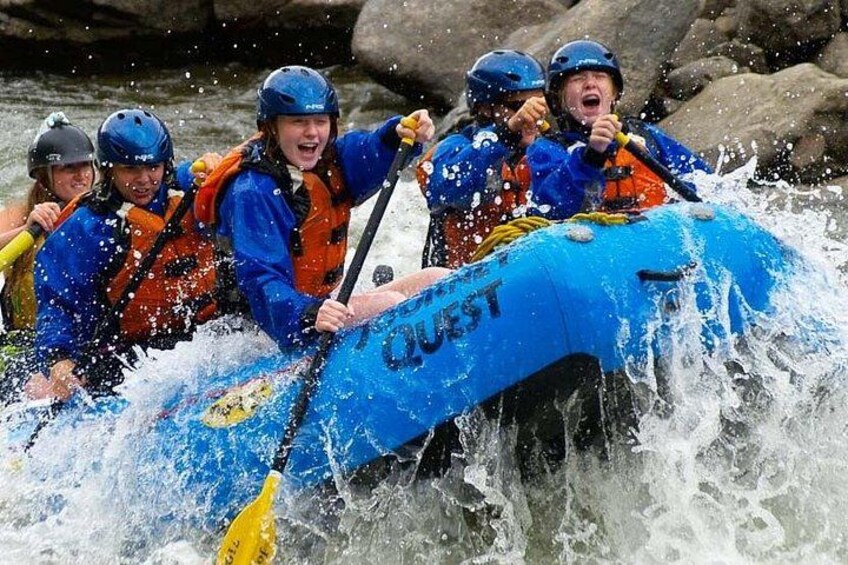 A group of people in a blue raft labeled 'QUEST' navigating through a river with rapids. 1