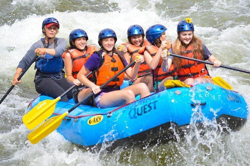 A group of people in a blue raft with the word 'QUEST' on it, paddling through a river. 4