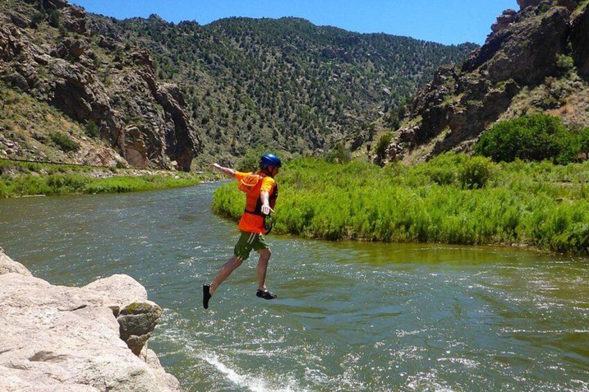 A person wading through a river in a natural landscape with rocky cliffs and greenery. 3