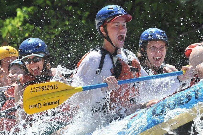 A group of people in a white and orange raft with a blue paddle, navigating through water. 2
