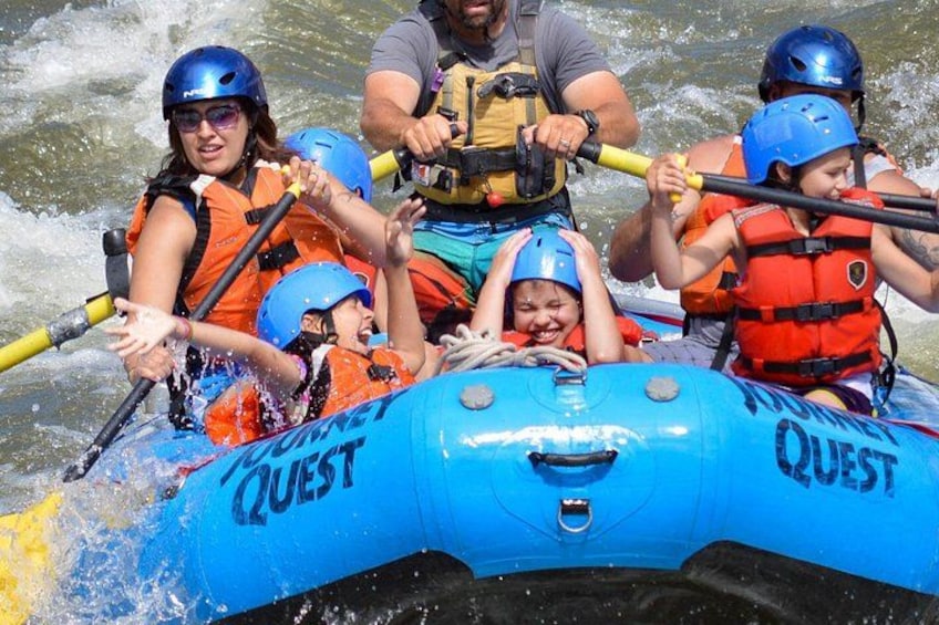 A group of people in a blue inflatable raft labeled 'QUEST' on a river. 5