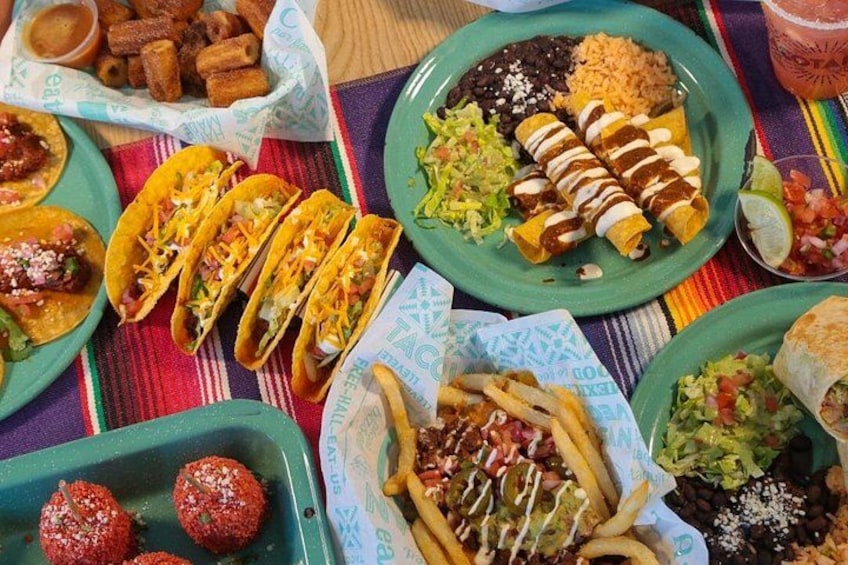 A variety of Mexican dishes including tacos, burritos, and enchiladas on a table with a colorful tablecloth. 2