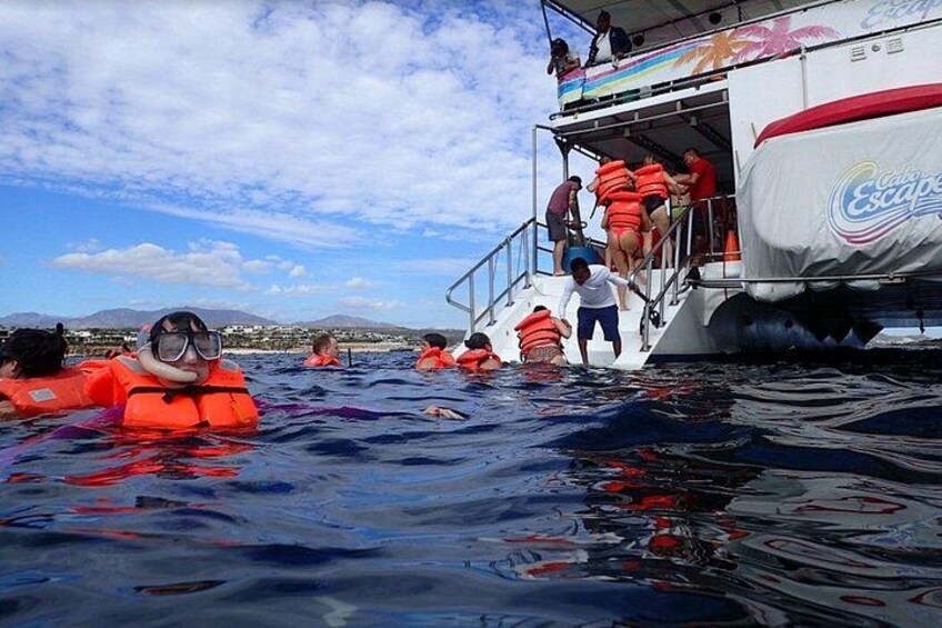 Mensen in het water met reddingsvesten, een boot met een rood-witte afdekking, en een heldere lucht. 2
