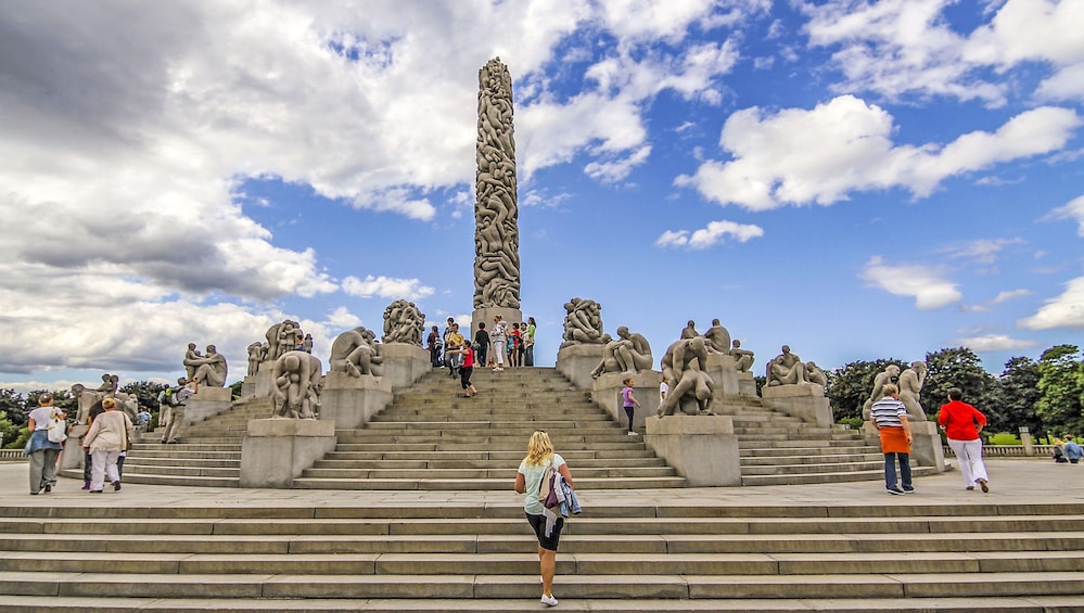 A sculpture of human figures on stairs with a tall column in the center. 1
