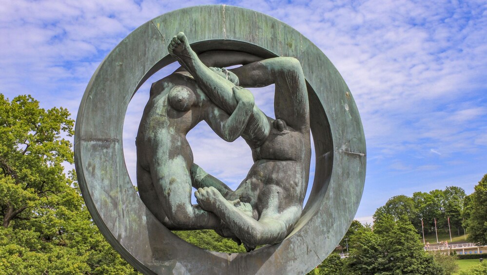 A large circular sculpture of intertwined human figures in a park. 2