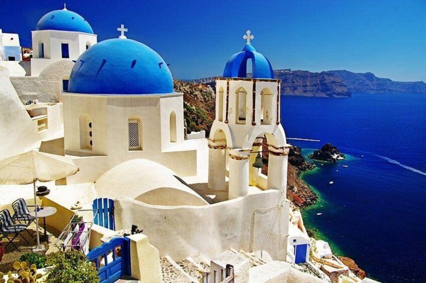Un pueblo costero con edificios blancos y cúpulas azules, un mar azul cristalino y una costa rocosa. 1