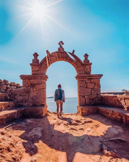 Una persona al peu d'una antiga arcada de pedra amb vista a una massa d'aigua. 1