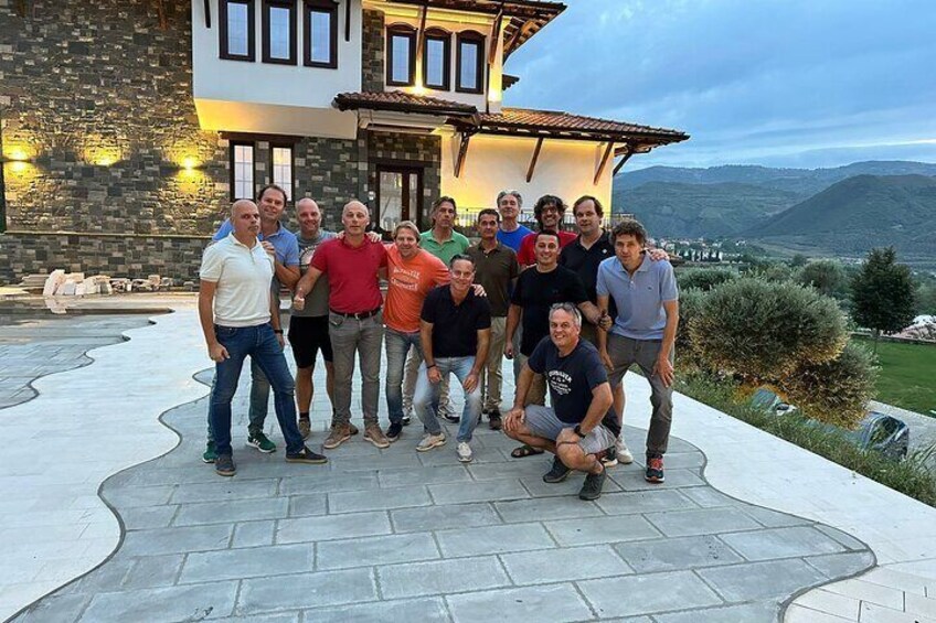 A group of people posing in front of a house with a stone facade and a view of the countryside. 1