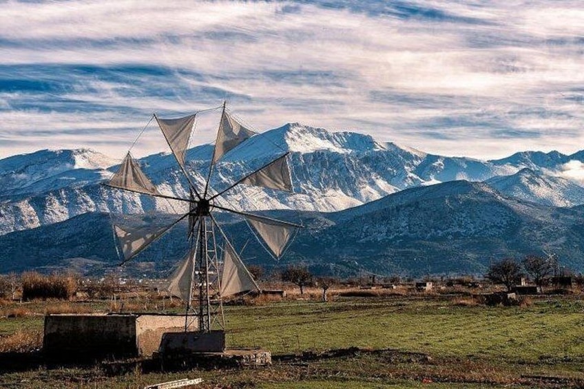 A windmill in a field with mountains in the background. 1