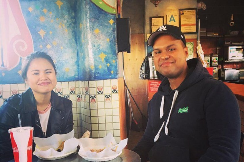 Dos personas sentadas en una mesa con recipientes de comida y una bebida. 5